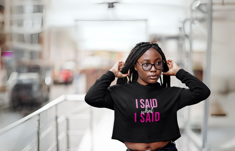 A woman walking carrying a coffee cup and wearing a black hoodie with the phrase believe in you